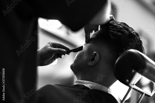 Vintage black and white photo of shaving beard in barber shop. Barber does his job.