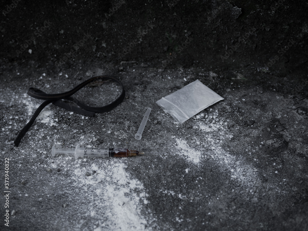 Heroin in syringe and powder heroin in plastic bag pack with rubber band on dirty cement floor. Addictive substance or narcotic concept. Heroin in syringe and powder heroin in plastic bag pack with rubber band on dirty cement floor. Addictive substance or narcotic concept.