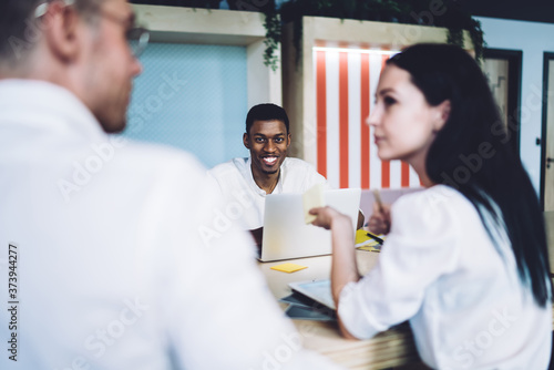 Positive African American worker using laptop while coworkers having discussion at meeting