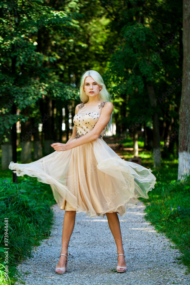 Young beautiful blonde girl in beige dress, summer park outdoor