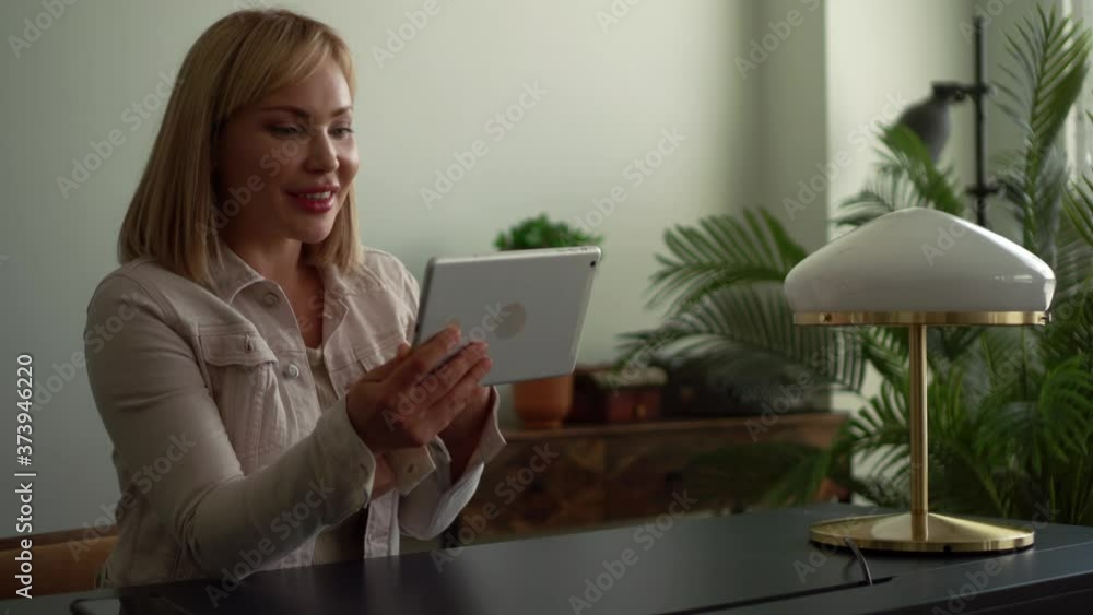 smart blonde woman is communicating online by tablet with internet, sitting at home, talking and explaining smart blonde woman is communicating online by tablet with internet, sitting at home, talking and explaining