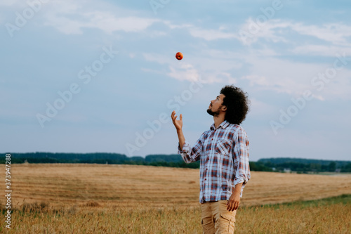 Latin american man in a field throwing an apple in the air 