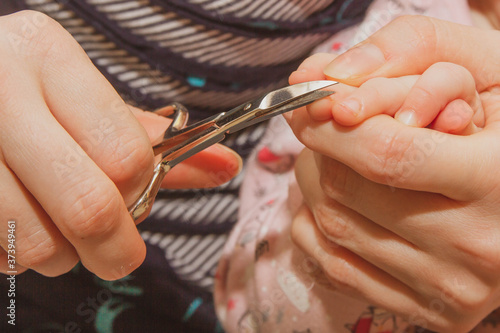 A mother cuts her nails with scissors for a small child. Care and care of parents for the baby.