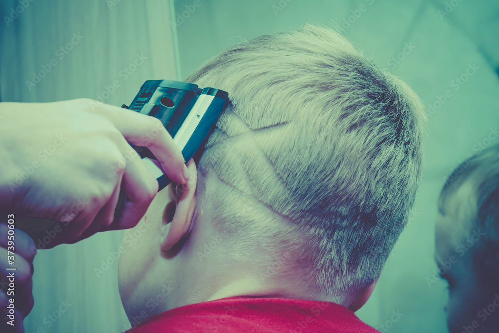 Naklejka premium Haircut of a European blond boy's hair with a hair clipper. The image on the head of a child, a person in the form of a spider's web.