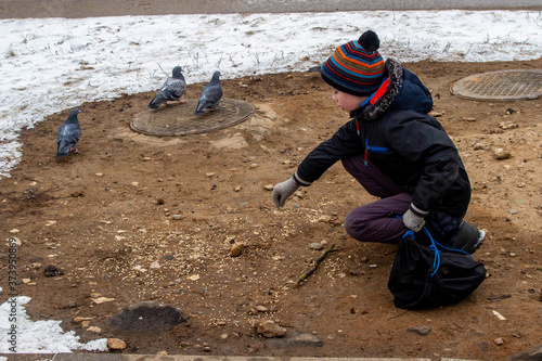 A teenage boy feeds pigeons in winter. A European child takes care of hungry birds.