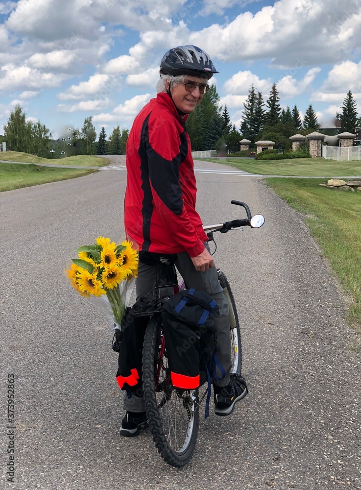 Obraz premium Senior riding a bike carrying sunflowers