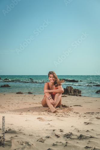 Beautiful young European woman with an orange swimsuit sitting on a beach in Cádiz