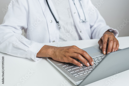 hands of an afro doctor using a modern laptop on the top of a white desk