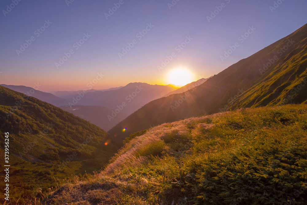 A scenic sunset in the mountains with sunlight, beautiful light. Evening summer landscape in a valley with horizon, sky, grass, flowers