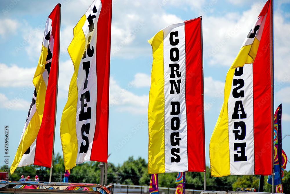 Obraz premium Bright yellow and red banners on poles advertising food for sale at a county fair