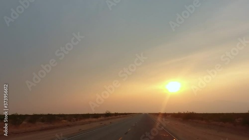 Driving down a road in the countryside towards the setting sun in a flat, featureless desert landscape