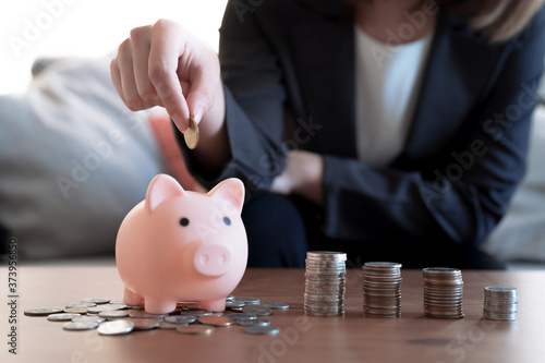 Business woman in a suit is putting coins in a piggy bank to save money, Focus on her hand, Financial concept.