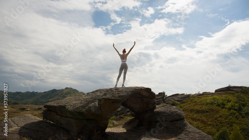 A girl in sportswear stands on top of a cliff. Back view.