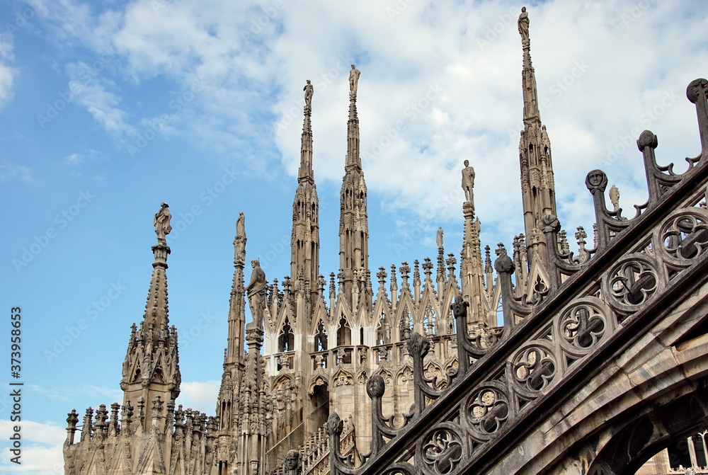 Statue on spire of Milan Cathedral on blue sky background, Milan, Italy. Detail of Gothic roof overlooking Milano city in summer. Nice view of Milan from above