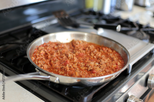 Bolognese sauce cooking in a stainless steel skillet.