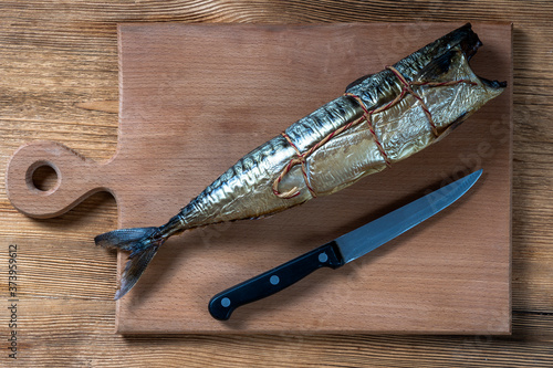 Hot smoked mackerel fish in the kitchen on wooden board with knife, top view, close up