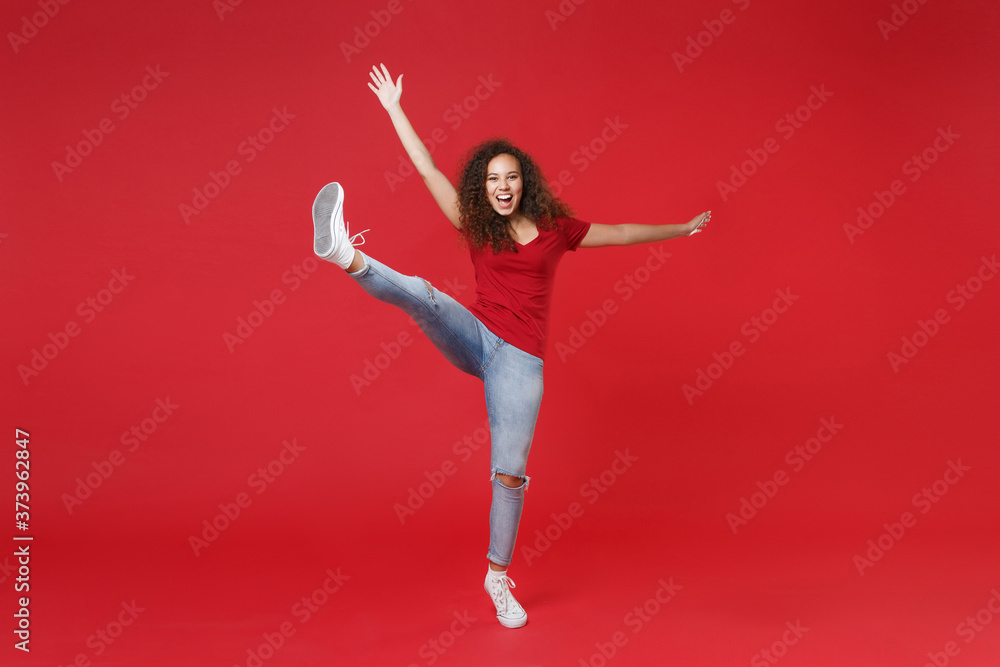 Full length portrait of excited young african american girl in casual t-shirt isolated on red background studio portrait. People lifestyle concept. Mock up copy space. Rising spreading hands and legs. Full length portrait of excited young african american girl in casual t-shirt isolated on red background studio portrait. People lifestyle concept. Mock up copy space. Rising spreading hands and legs.