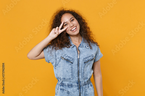 Smiling young african american woman girl in casual denim clothes isolated on yellow background studio portrait. People sincere emotions lifestyle concept. Mock up copy space. Showing victory sign.