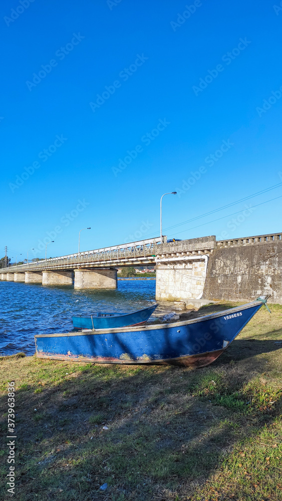 Local fishing boats moored on the shoreline of the Cavado River in Fao, Esposende, Portugal, with the Fao metallic bridge, known as D. Luís Filipe Bridge.
