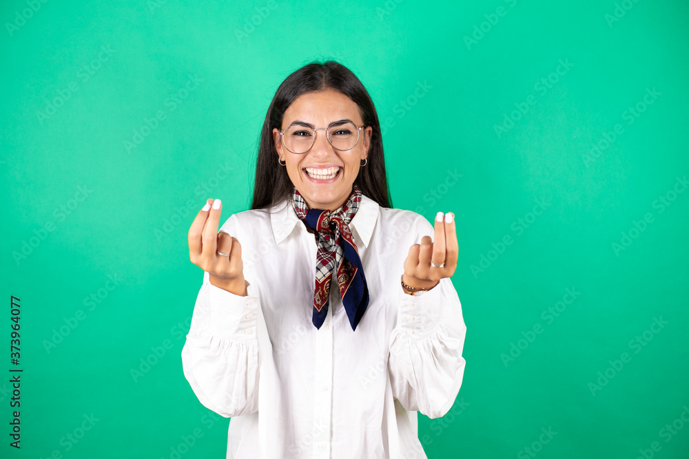 Young beautiful business woman over isolated green background doing money gesture with hands, asking for salary payment, millionaire business Young beautiful business woman over isolated green background doing money gesture with hands, asking for salary payment, millionaire business