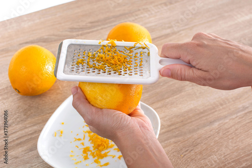 Принти на полотні Woman rubbing orange zest with metal grater in the kitchen