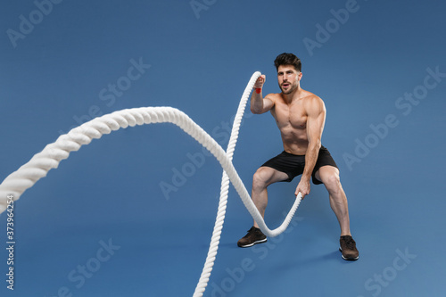 Fotografia Full length portrait of young bearded fitness sporty strong guy bare-chested muscular sportsman isolated on blue background