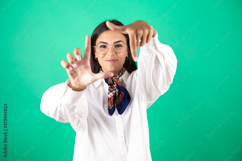 Naklejka premium Young beautiful business woman over isolated green background smiling making frame with hands and fingers with happy face