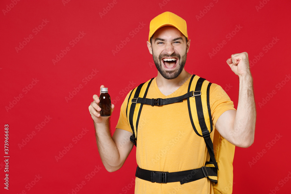 Delivery man in yellow cap t-shirt uniform thermal bag backpack with food hold tablets drugs isolated on red background studio Guy male employee work as courier of service coronavirus covid-19 virus Delivery man in yellow cap t-shirt uniform thermal bag backpack with food hold tablets drugs isolated on red background studio Guy male employee work as courier of service coronavirus covid-19 virus