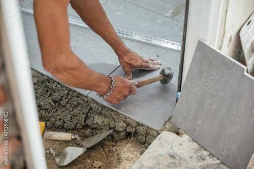 Hand of tiler laying and use mallet knocking granite tile on floor