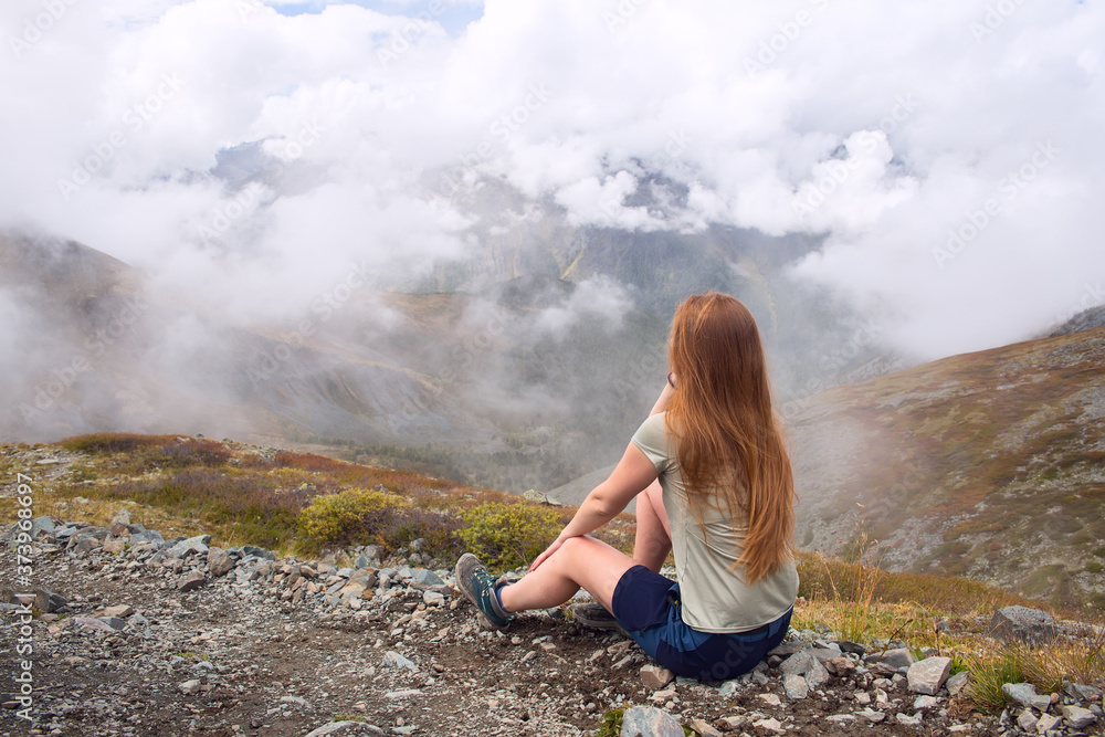 Young woman looks at mountains and clouds. Travel and tourism concept.