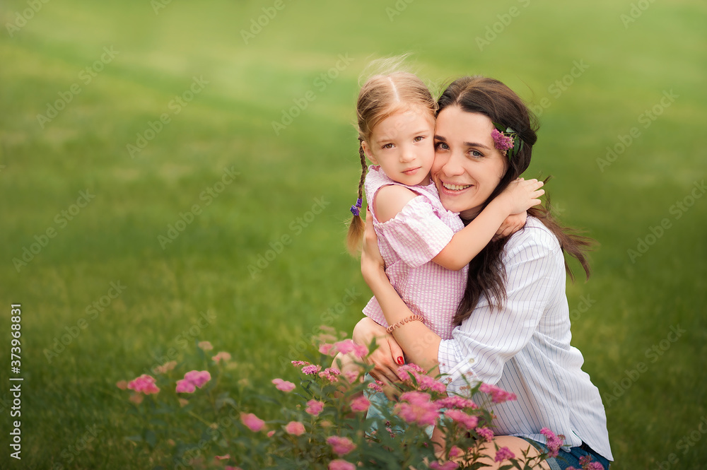 Mom and daughter with flowers close-up and copy space. Sisters near blooming flower beds in nature. Mom and daughter with flowers close-up and copy space. Sisters near blooming flower beds in nature.