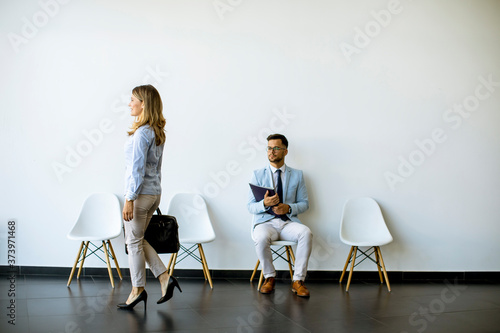 Businesswoman passing by young man sitting in the waiting room with a folder in hand before an interview
