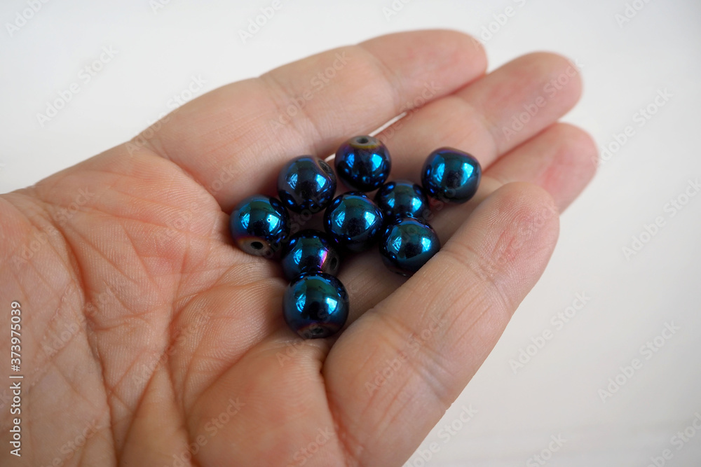 lots of blue hematite beads in your hand on a white background .natural mineral stones for needlework lots of blue hematite beads in your hand on a white background .natural mineral stones for needlework