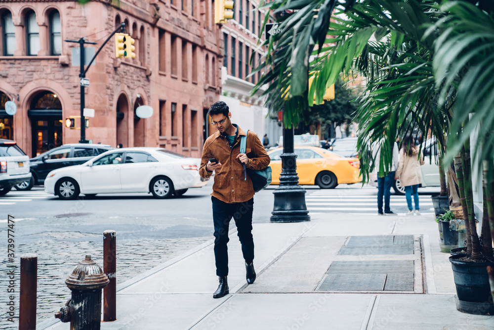 Modern ethnic young man using smartphone and walking along street Modern ethnic young man using smartphone and walking along street