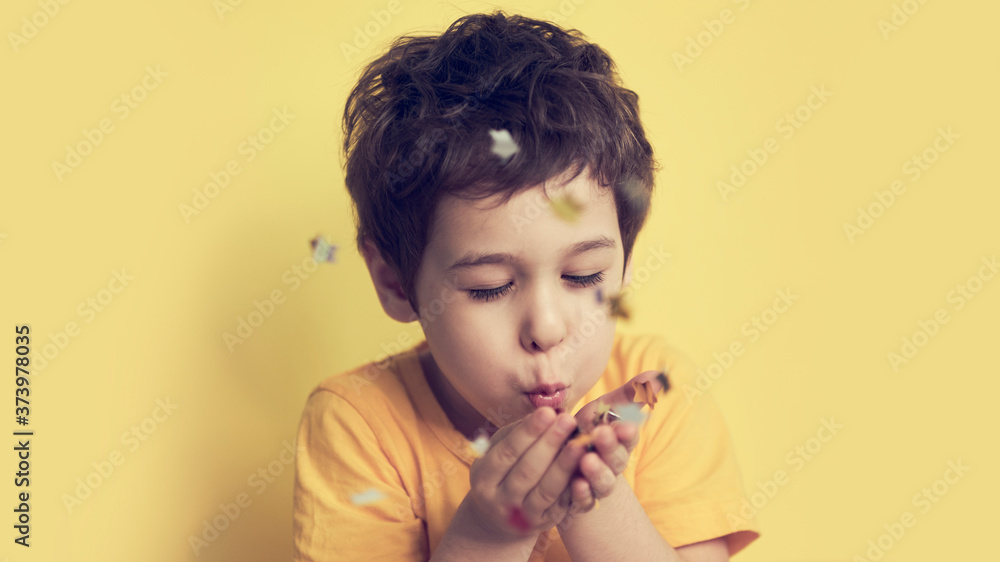 happy birthday child. Photo of charming cute fascinating nice little boy blowing confetti at you to show her festive mood with emotional face expression. happy birthday child. Photo of charming cute fascinating nice little boy blowing confetti at you to show her festive mood with emotional face expression.