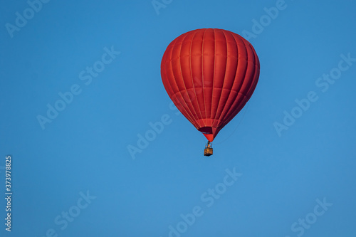 Bright red hot air balloon in flight against a background of blue sky. Colorful watercolor painting balloon flying high. Close-up.
