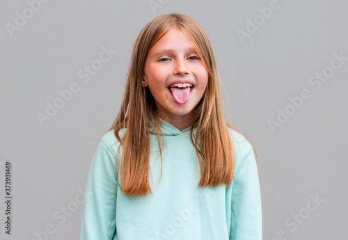 Funny cute young girl smiling winking showing tongue looking at camera over gray background.