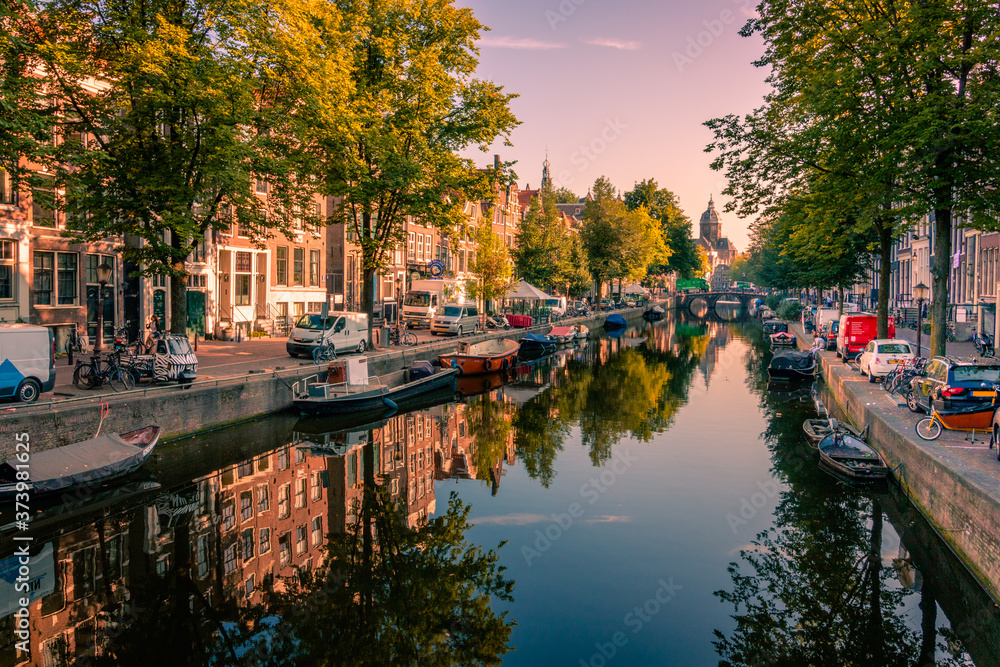 Picturesque houses and their reflection in a canal in Amsterdam at sunset