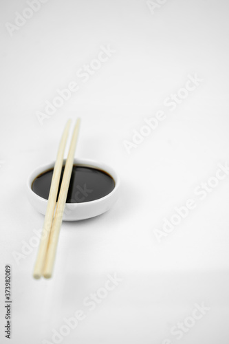 soy sauce in a small white bowl and bamboo chopsticks, isolated on white