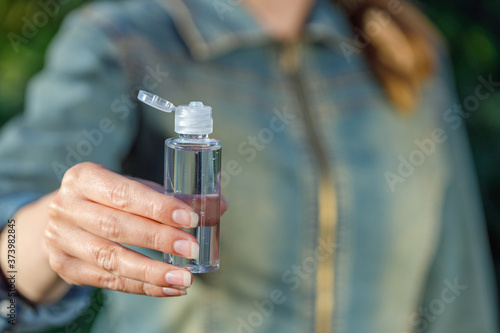 A woman holds a bottle with antiseptic antibacterial gel in her hands. Close-up hand in focus. The background is blurred.