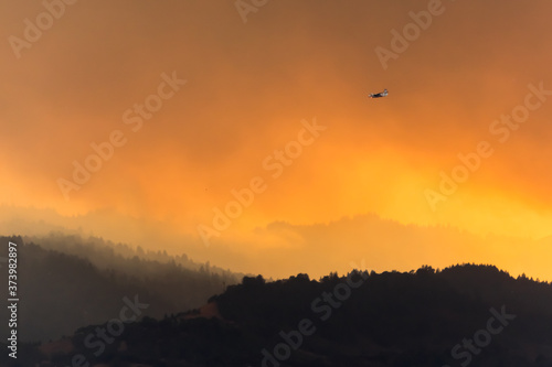 Heroes Fly Here - Fire aircraft returns to Sonoma County (CA) Airport against smoke backlit by the setting sun. Santa Rosa, California, USA