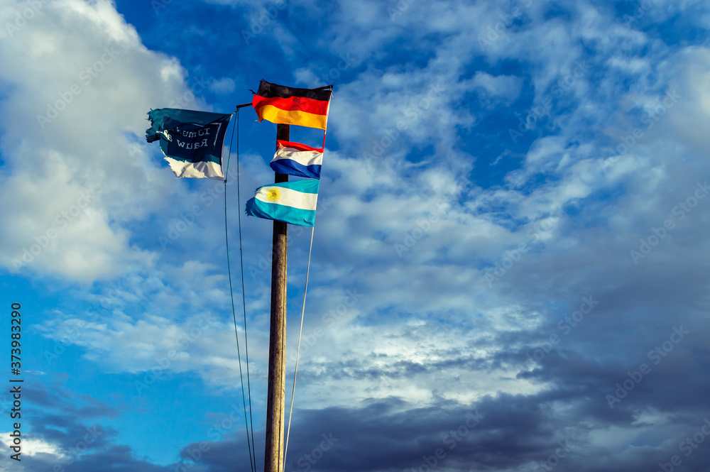 Wooden flagpole with the German, Dutch and the Argetina flag. And the welcome flag of the little Dutch town Ijmuiden aan Zee. Slogan Text on the flag translation: Ijmuiden raw at Sea. Wooden flagpole with the German, Dutch and the Argetina flag. And the welcome flag of the little Dutch town Ijmuiden aan Zee. Slogan Text on the flag translation: Ijmuiden raw at Sea.