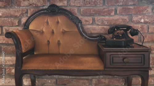 Elegant vintage old phone on elegant wooden and textile upholstery vintage sofa against brick wall antique decoration
