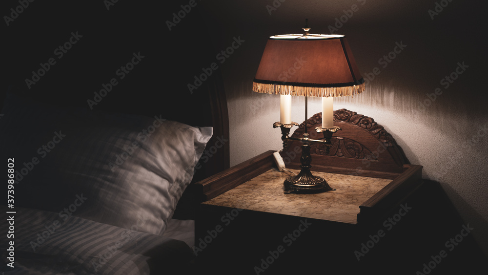 Bedside nightstand table with antique retro vintage lamp low key photography relaxing bedtime - obrazy, fototapety, plakaty 