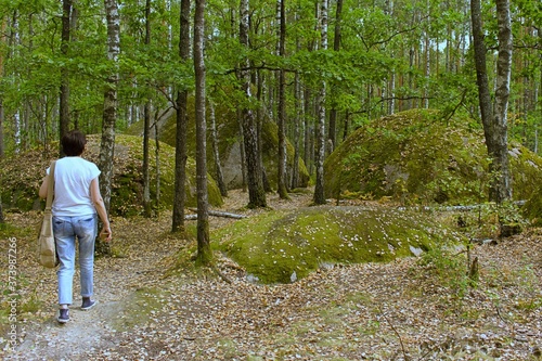 girl walks towards huge boulders covered with ancient moss in a green forest photo