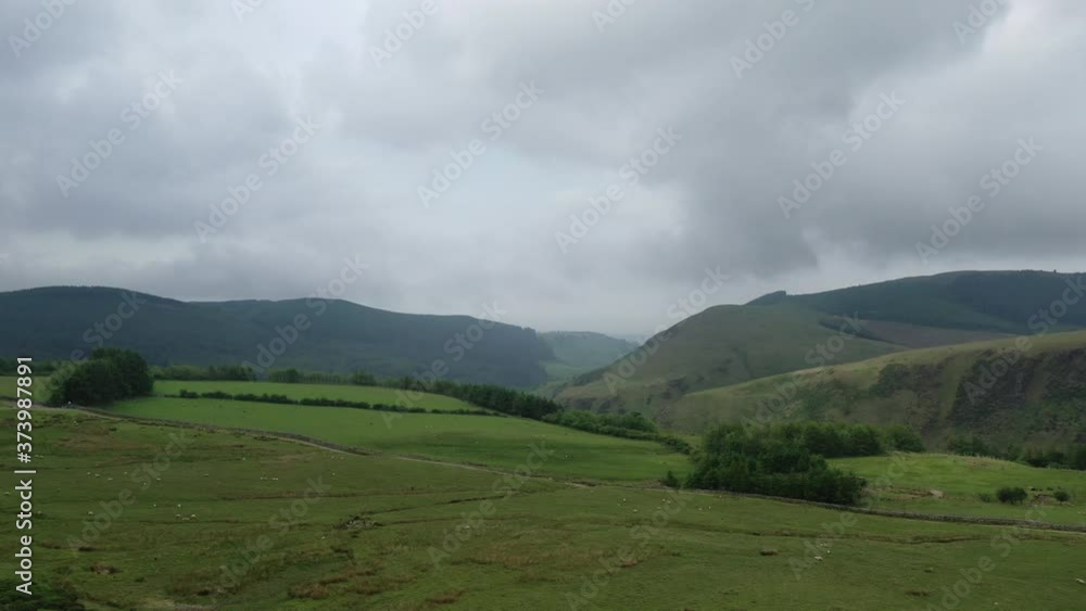 Aerial backwards shot of some green fields, surrounded by the mountains of the English Lake District.