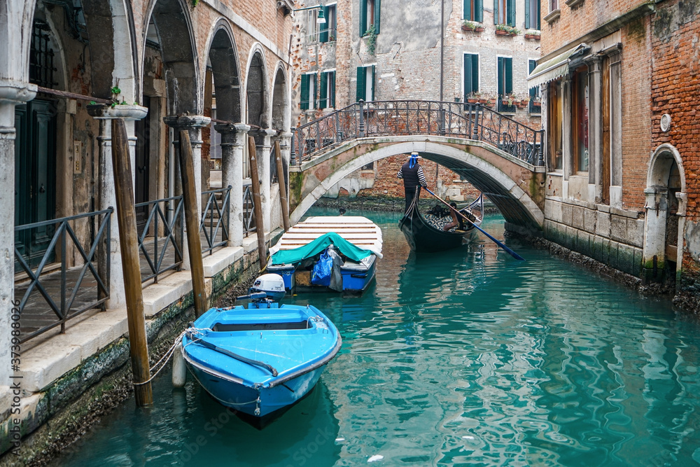 Gondolier riding a gondola under the beautiful Ponte del Piovan bridge in a Venetian water canal. At Venice, Italy