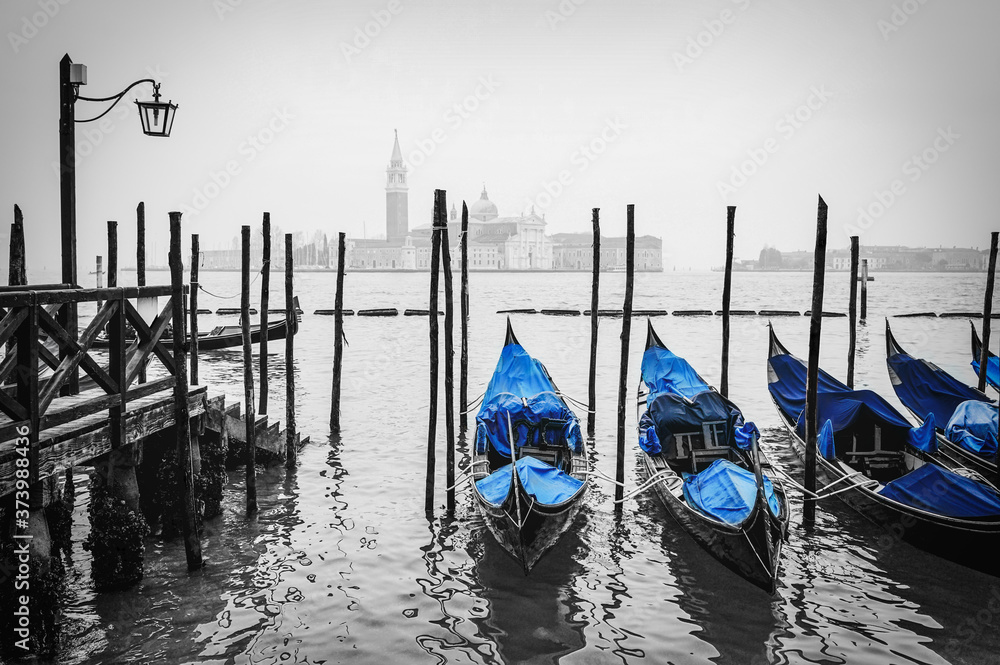 Typical gondolas stationed in old wooden dock with San Giorgio Maggiore cathedral in the distance. Venice, Italy