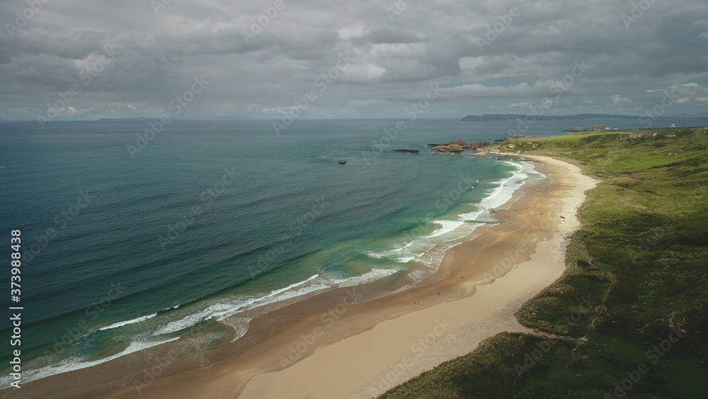 Aerial view sandy beach: ocean foamy waves drops to coastline in White Beach, Antrim County. Seascape of picturesque nature of Northern Ireland. Dramatic summer scenery in day