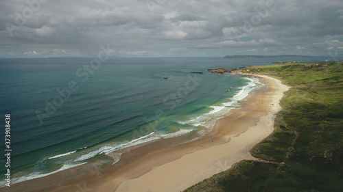 Aerial view sandy beach  ocean foamy waves drops to coastline in White Beach  Antrim County. Seascape of picturesque nature of Northern Ireland. Dramatic summer scenery in day